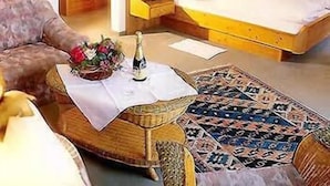 Um quarto com uma cama, uma mesinha com um frasco e flores, um tapete estampado e um sofá.