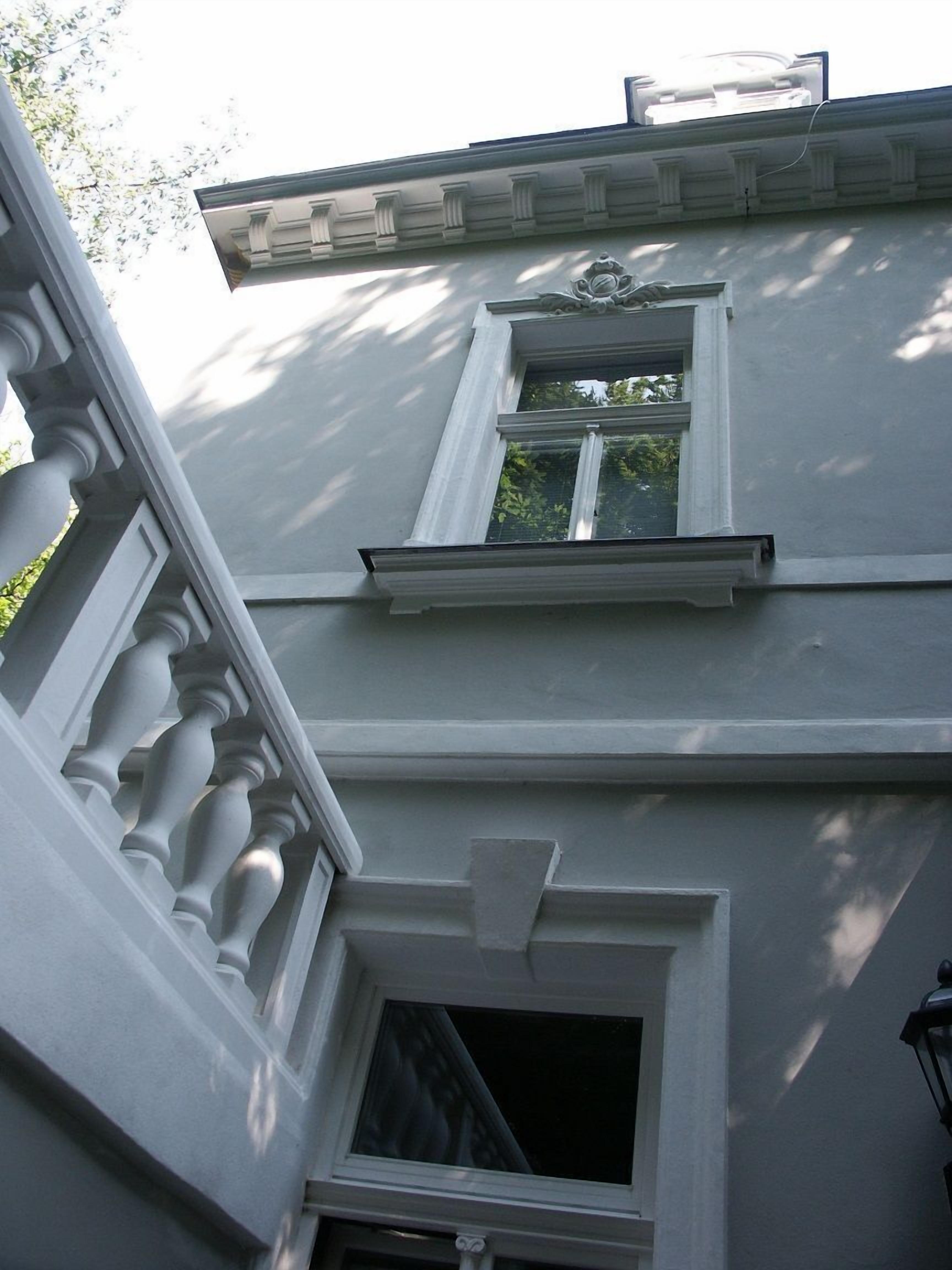 A two-story building with a symmetrical facade, featuring a central window with a decorative lintel, a smaller window on the upper floor, and a door with a transom window.