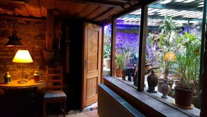 Un cuarto acogedor con un banco de madera, una mesa con una lámpara y vistas a un jardín a través de una ventana con plantas en macetas.