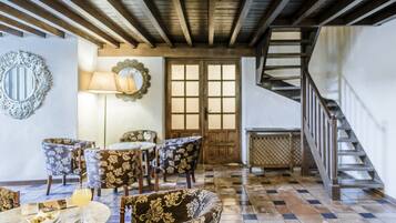 A dining area with floral-patterned chairs, a round table, and a lamp. A staircase is visible to the right.
