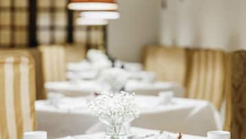 A dining area with tables set for service, a vase of flowers, and striped upholstered chairs.