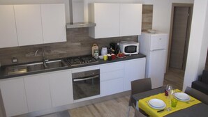 Una cocina compacta con armarios blancos, un microondas, una estufa y un refrigerador. Hay una mesa de comedor con mantel amarillo y platos para dos.