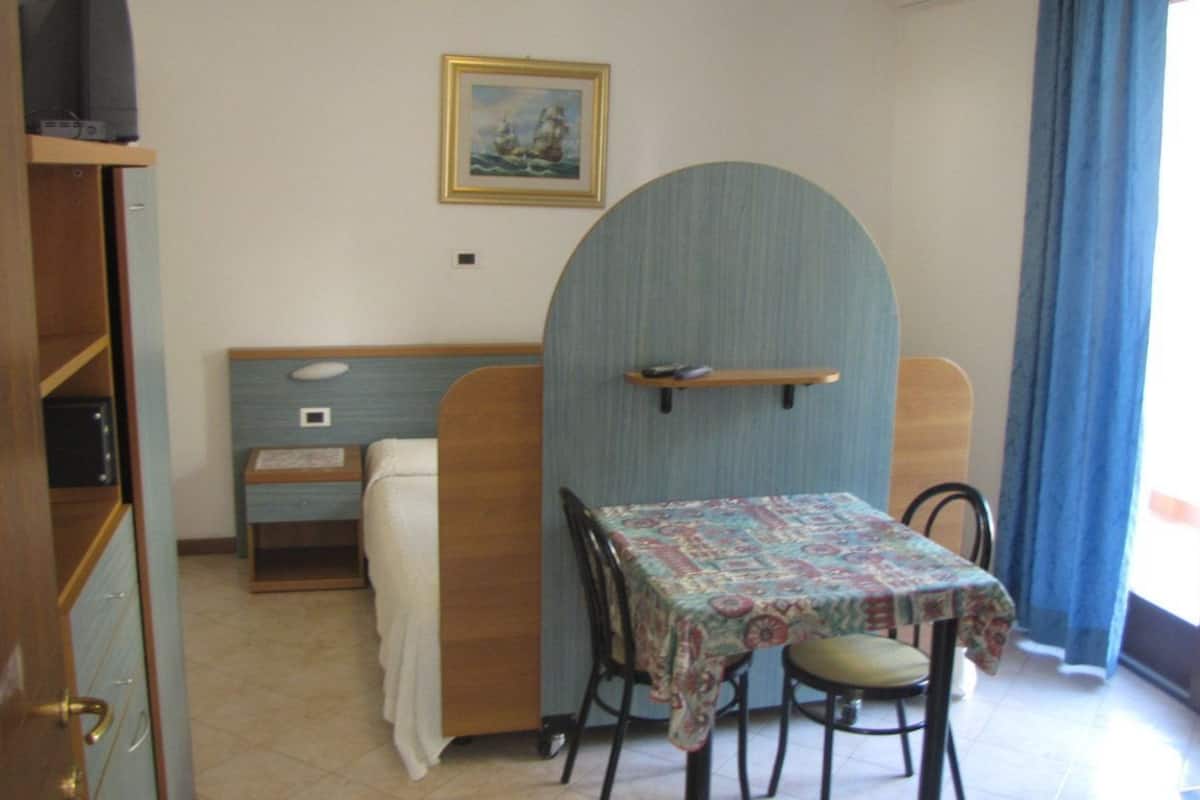 A small dining area with a table and chairs, a blue wall, a painting, and a window with curtains.