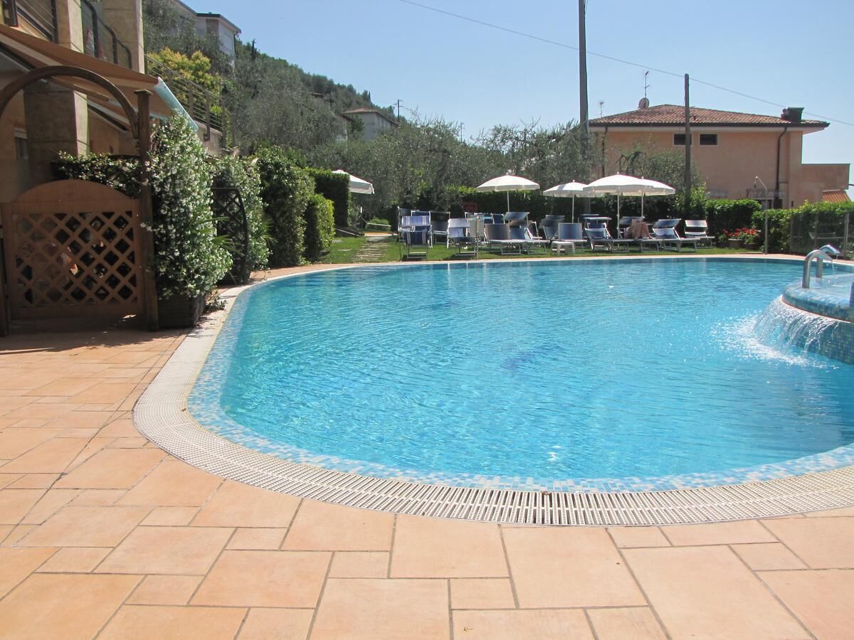 Una piscina con sillones de descanso y sombrillas, rodeada de un patio empinado y vegetación.