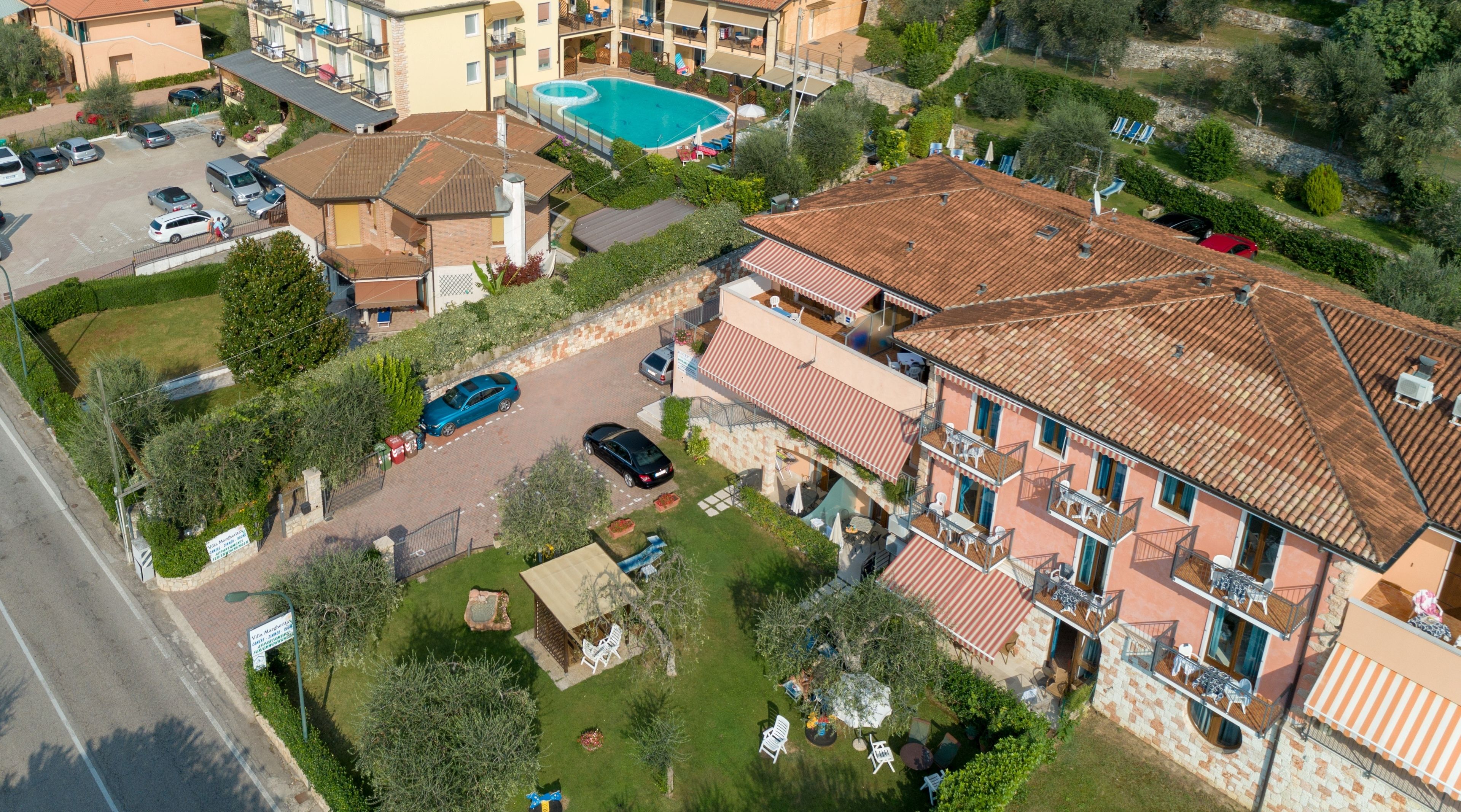 An aerial view of a residential area with a large building featuring a tiled roof, a swimming pool, and a parking area.