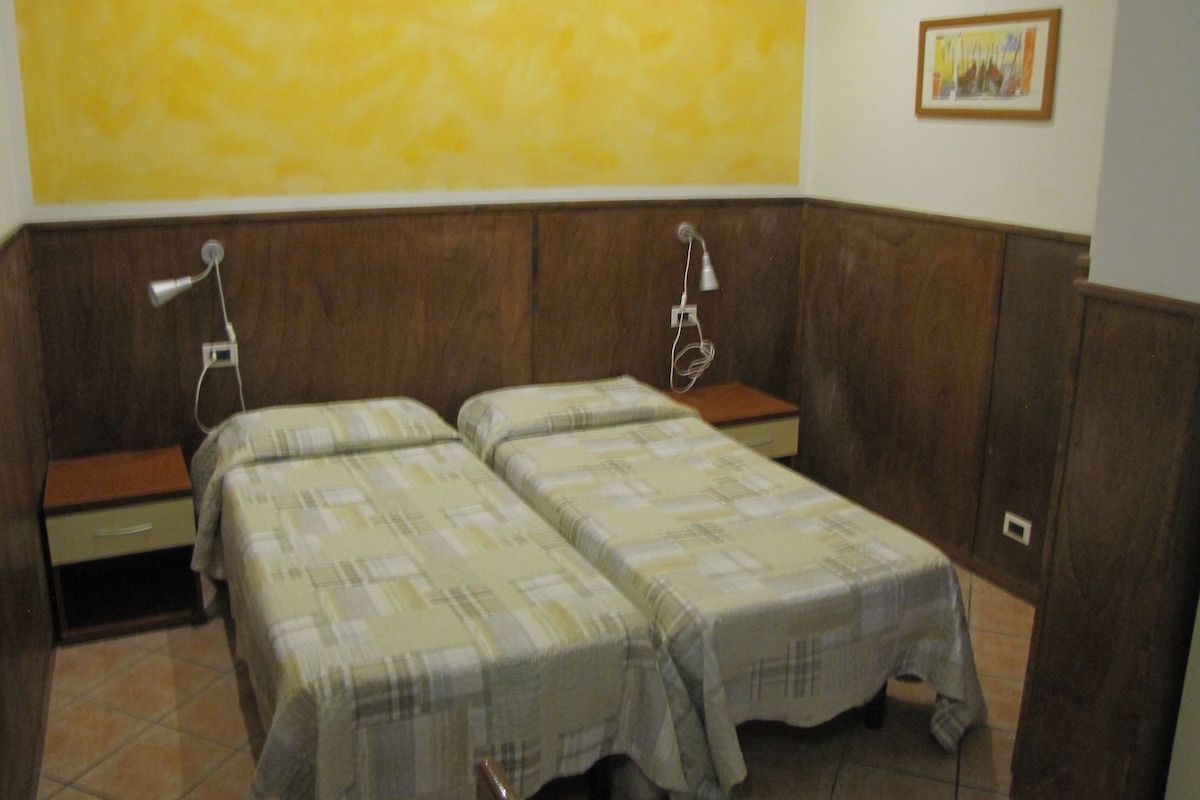 A room with two beds, wooden paneling on the walls, a small table, and a single lamp.