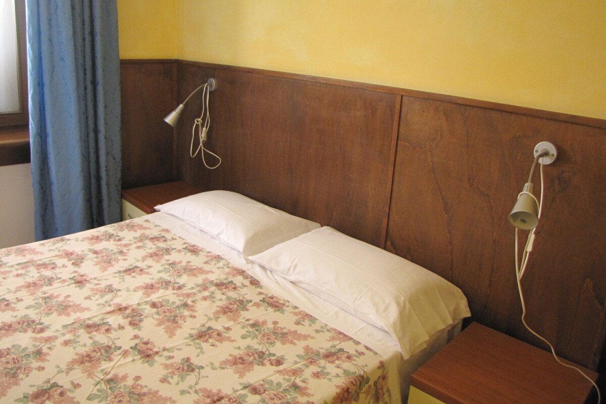 A single bed with a floral bedspread, a wooden headboard, and a bedside lamp.