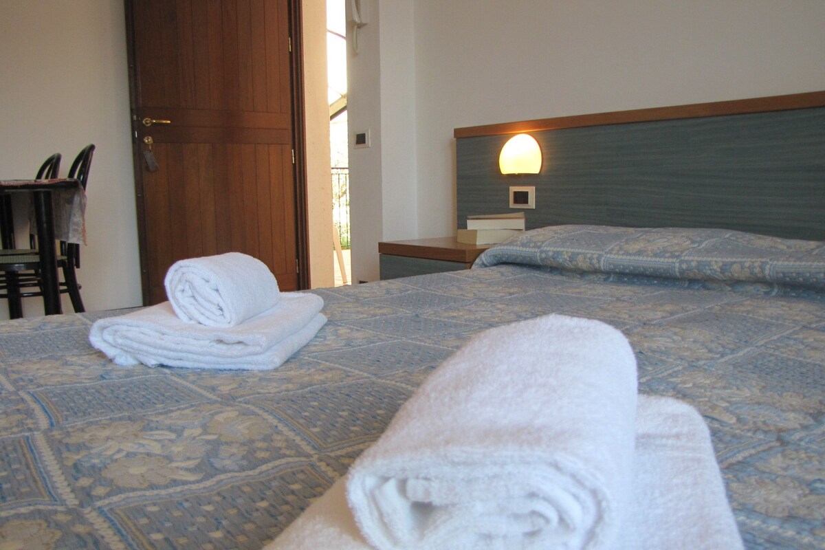 A hotel room with a bed, a nightstand, a chair, and a door.
