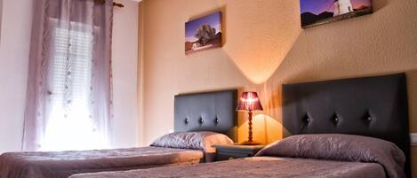 Habitación de hotel con dos camas, una mesita de noche, una lámpara y una obra de arte en la pared que muestra un molino y un árbol.