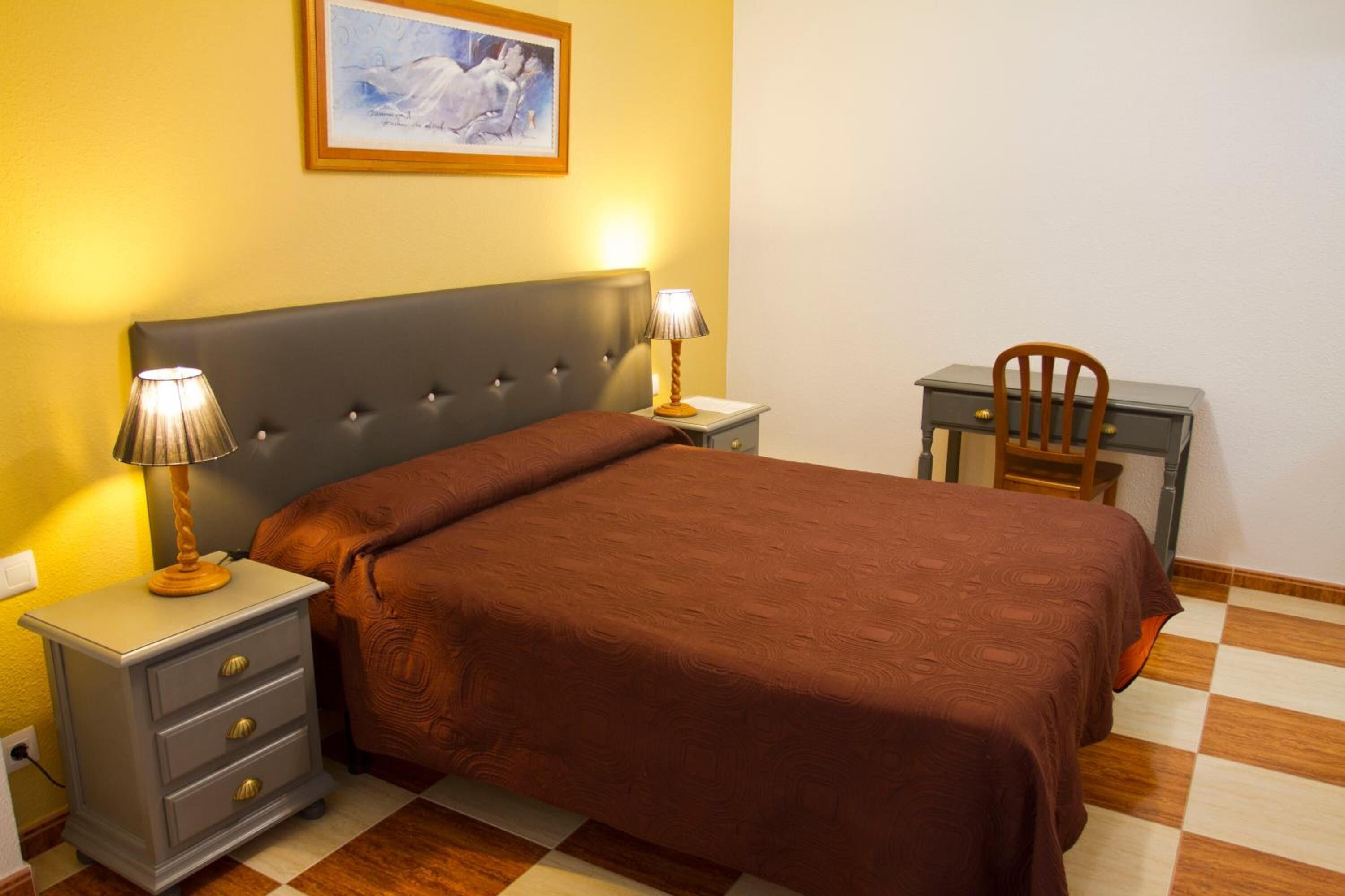 A bedroom with a bed, two bedside tables, a chair, and a painting on the wall.