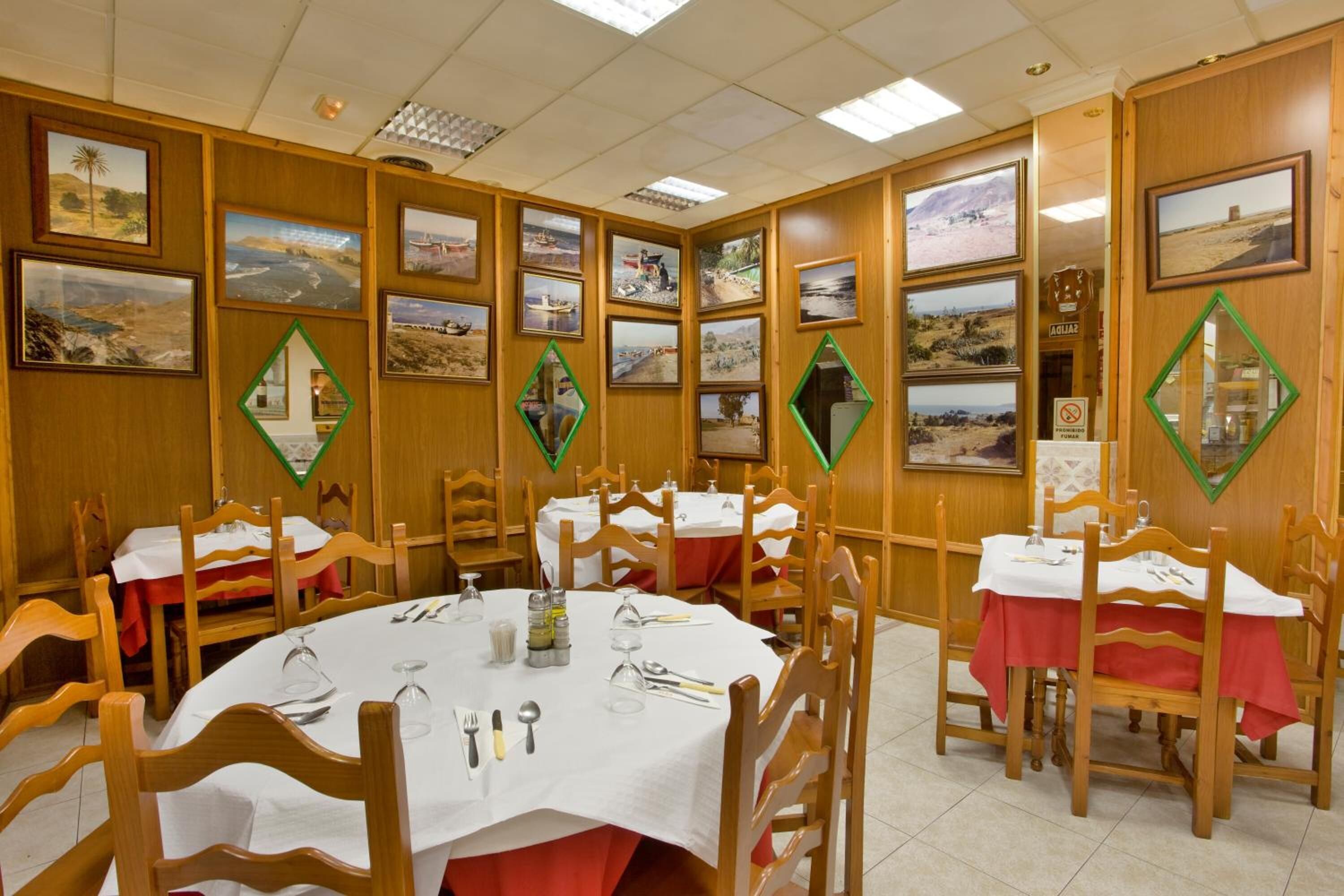 A dining area with wooden walls, framed pictures, and tables set for four.