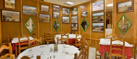 A dining area with wooden walls, framed pictures, and tables set for four.