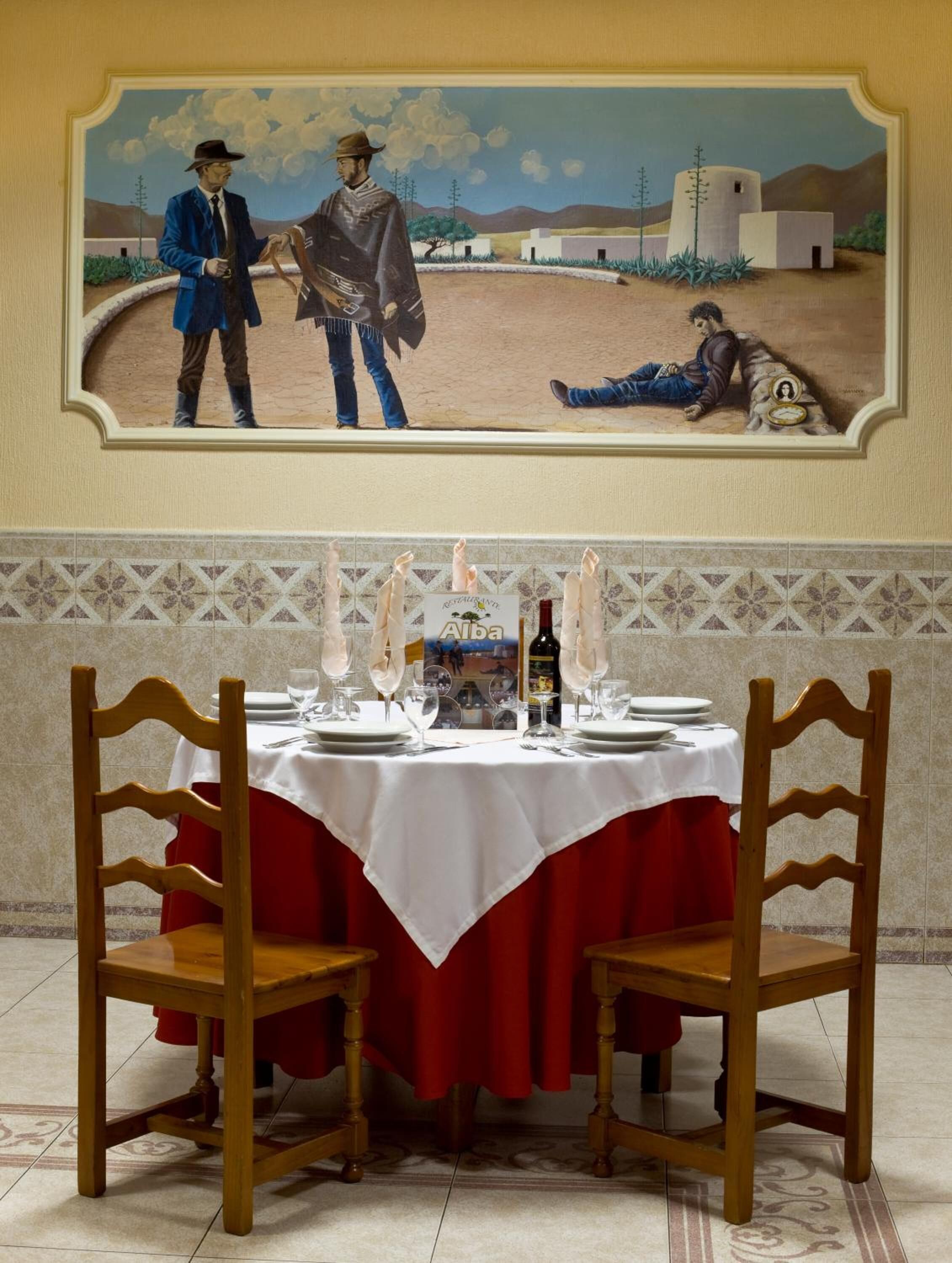 A dining area with a table set for two, a painting above the table, and a tiled floor.