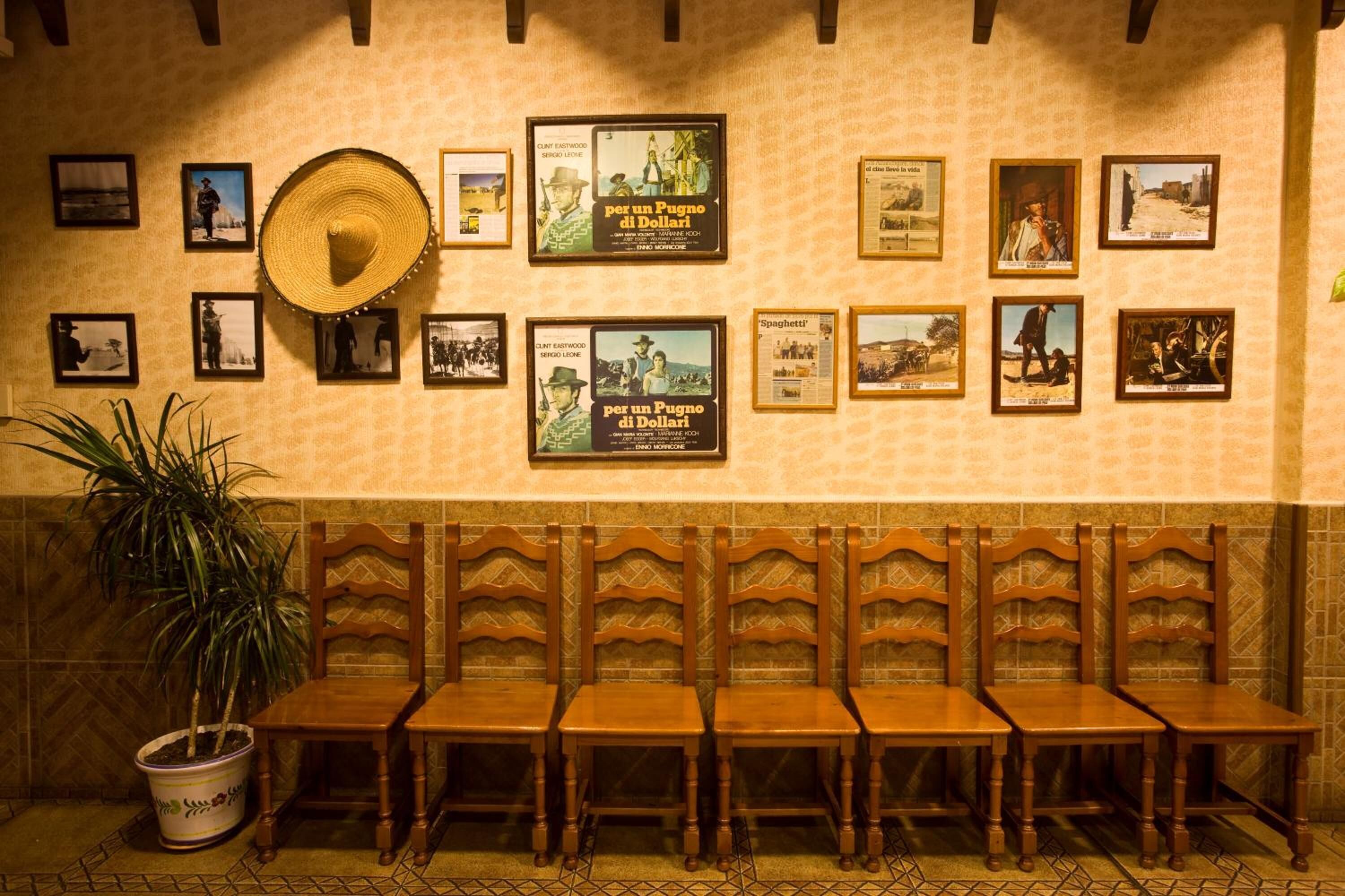 A restaurant with wooden chairs and tables, a large hat on the wall, and framed pictures on the wall.