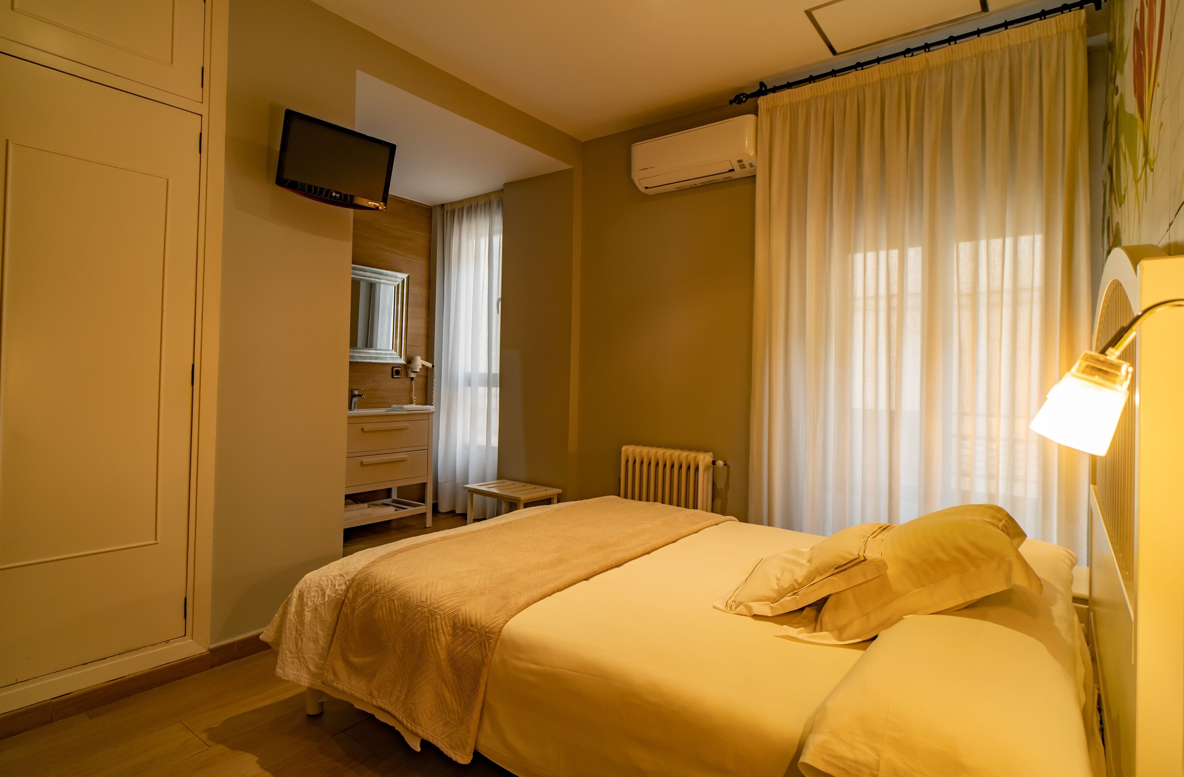 A hotel room with a bed, a television, a radiator, and a window with curtains.