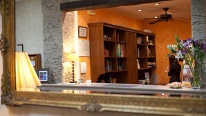 Zona de recepción con pared de piedra, mostrador de madera, estantería y ventilador de techo.