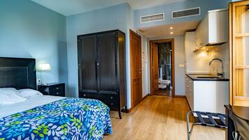 A hotel room with a bed, a wardrobe, a desk with a chair, a sink, and a view of the bathroom.