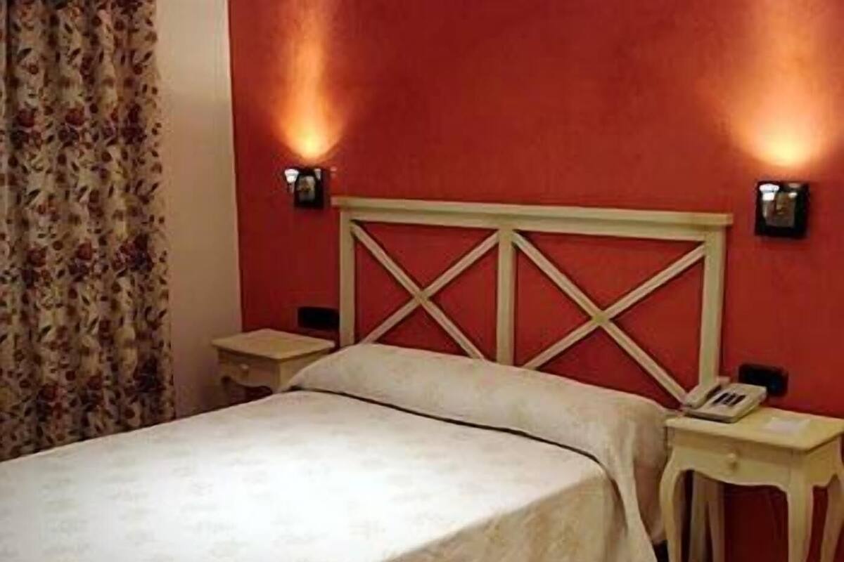 A bed with a wooden headboard, two bedside tables, and a wall-mounted light fixture.