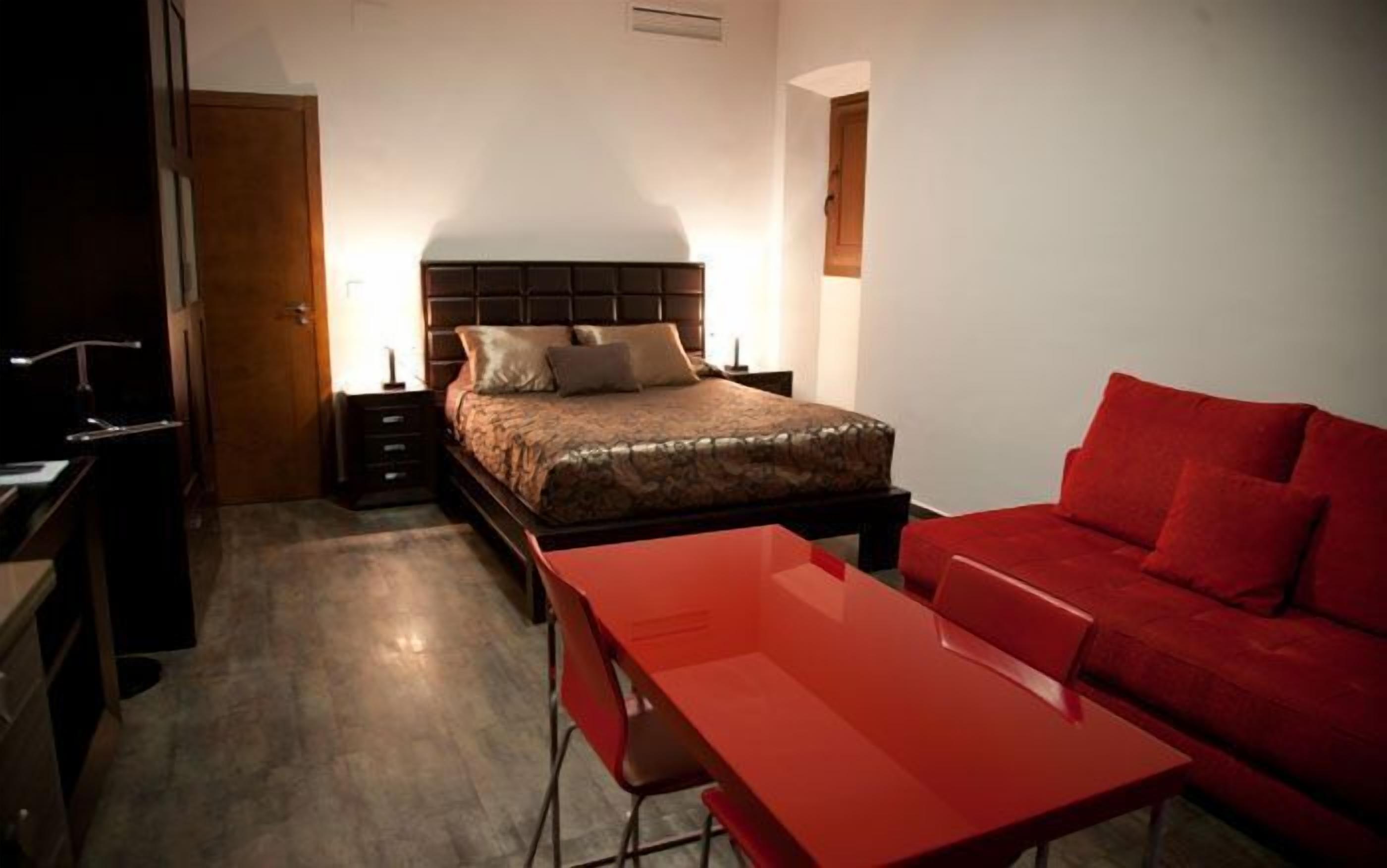Un dormitorio con una cama, un sofá rojo, un escritorio y una silla.