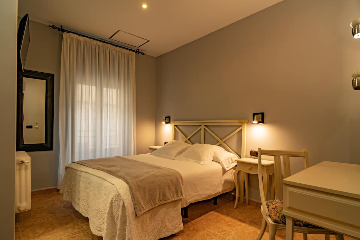 A bedroom with a bed, bedside table, chair, and a desk.