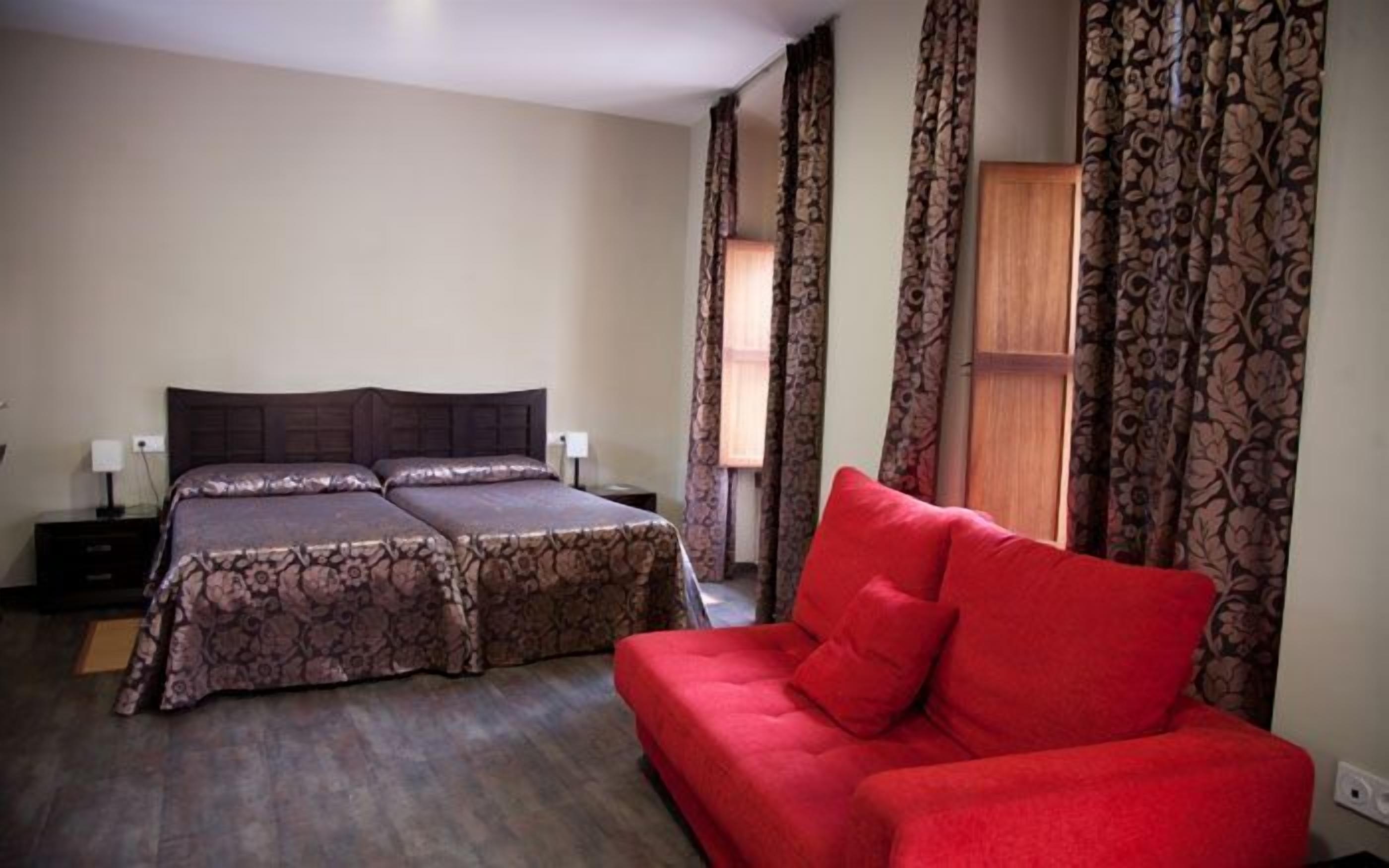 Un dormitorio con cama doble, sofá rojo y cortinas estampadas.