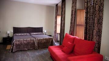 Un dormitorio con cama doble, sofá rojo y cortinas estampadas.