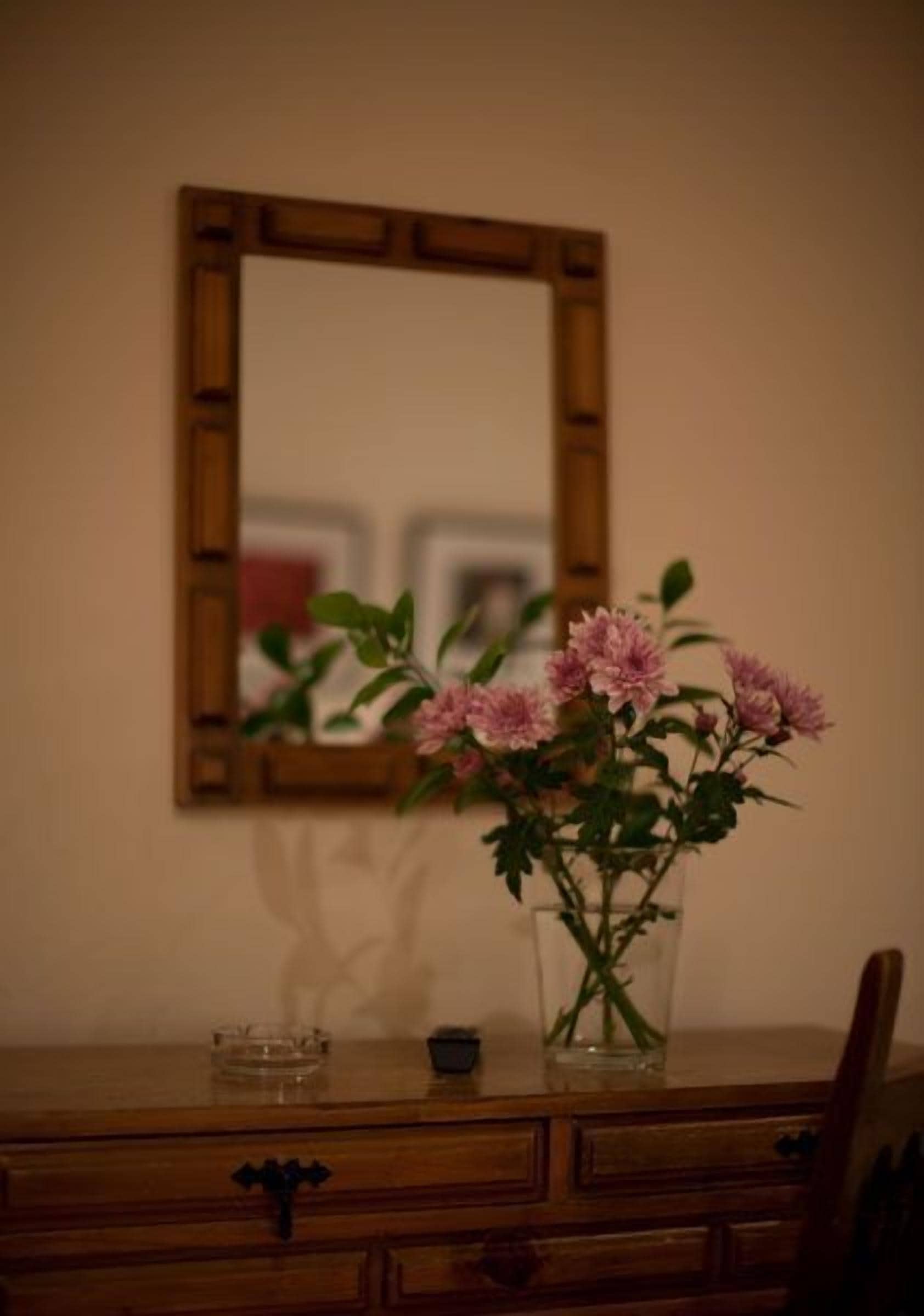 A wooden dresser with a vase of pink flowers on top.