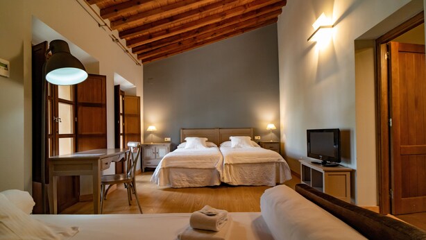 Habitación de hotel con dos camas, un escritorio, una silla, un televisor y techo de madera.