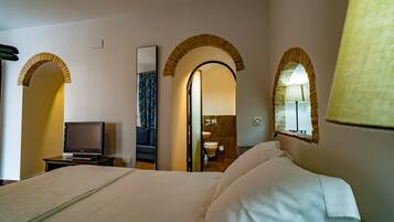 Habitación de hotel con cama, televisión y baño visible a través de un arco.