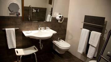 Un baño moderno con lavamanos, inodoro y bidé. Hay un taburete pequeño y un perchero para toallas.