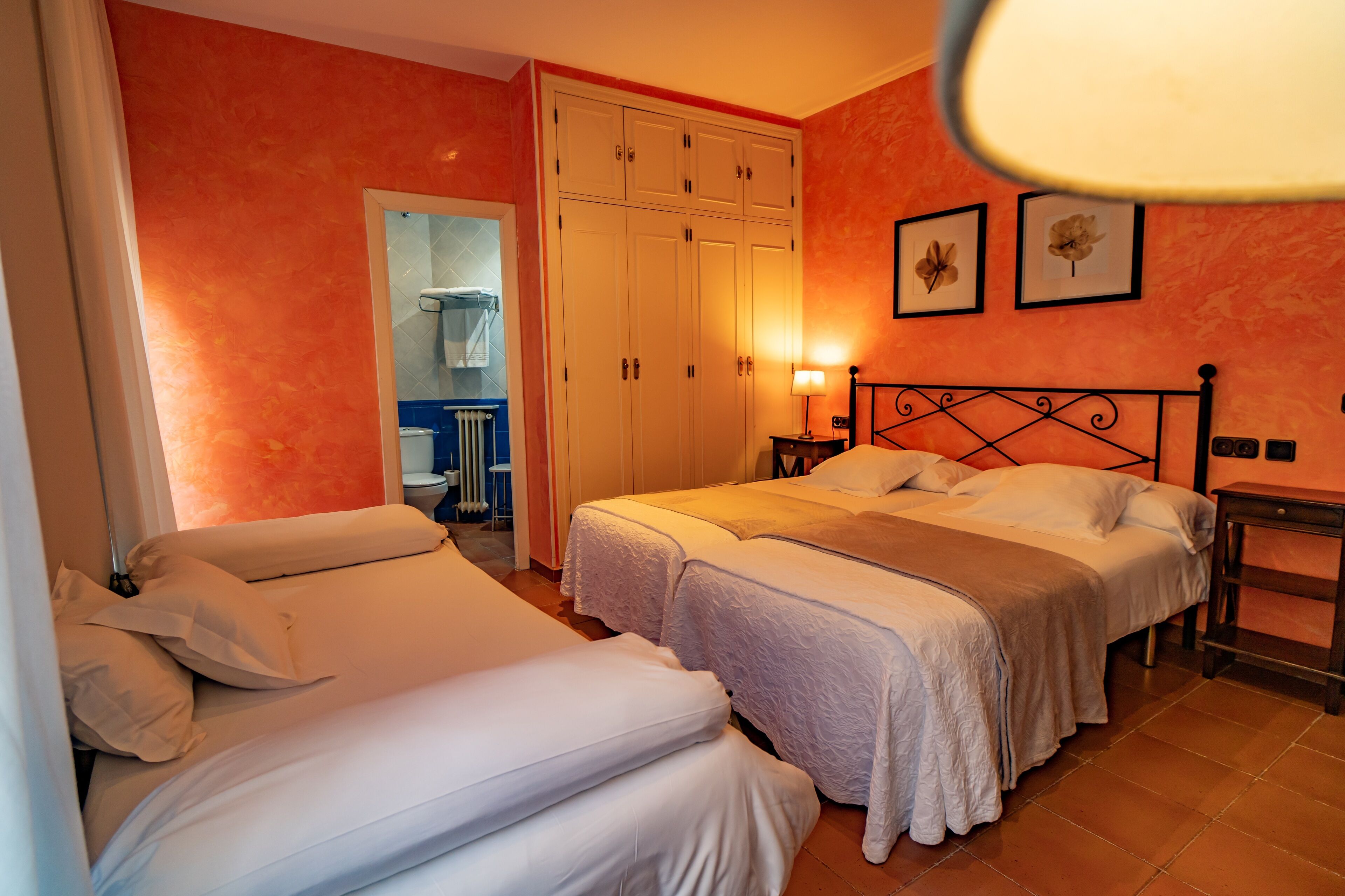 Habitación de hotel con dos camas, un armario, un baño y dos cuadros en la pared.