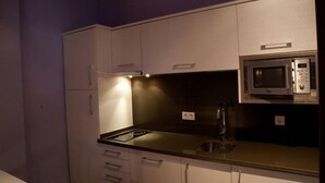Una cocina compacta con armarios blancos, un microondas de acero inoxidable y un lavamanos.