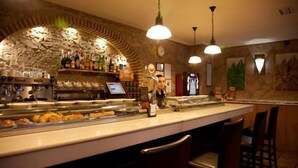 Un restaurante con un arco de piedra, una barra con pasteles y lámparas colgantes.