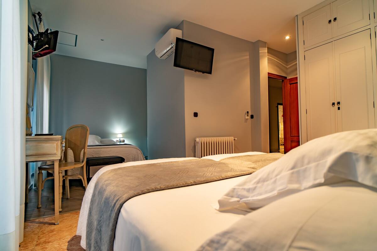 A bedroom with a bed, a desk, a chair, a TV mounted on the wall, and a wardrobe.
