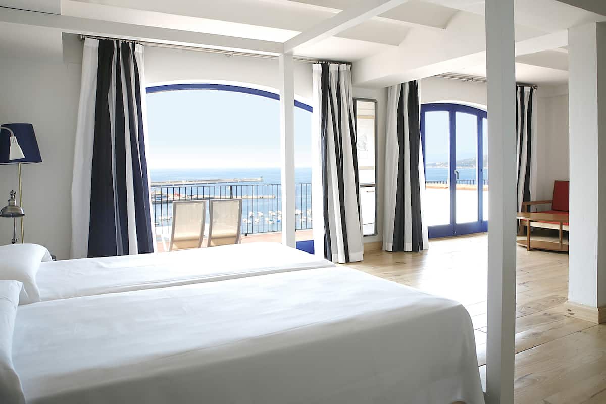 A hotel room with two beds, a balcony with a view of the sea, and a dining area.