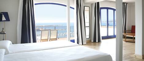 A hotel room with two beds, a balcony with a view of the sea, and a dining area.