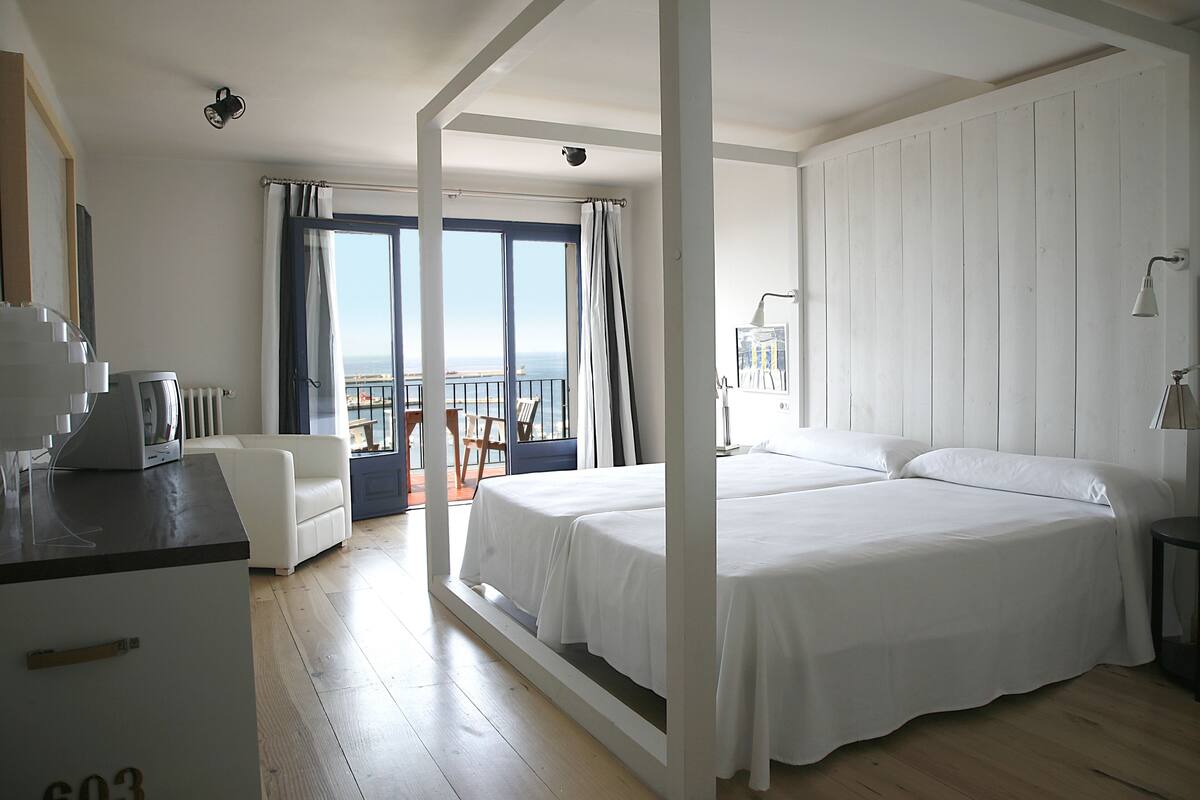A hotel room with a balcony, a bed, a desk, and a view of the sea.