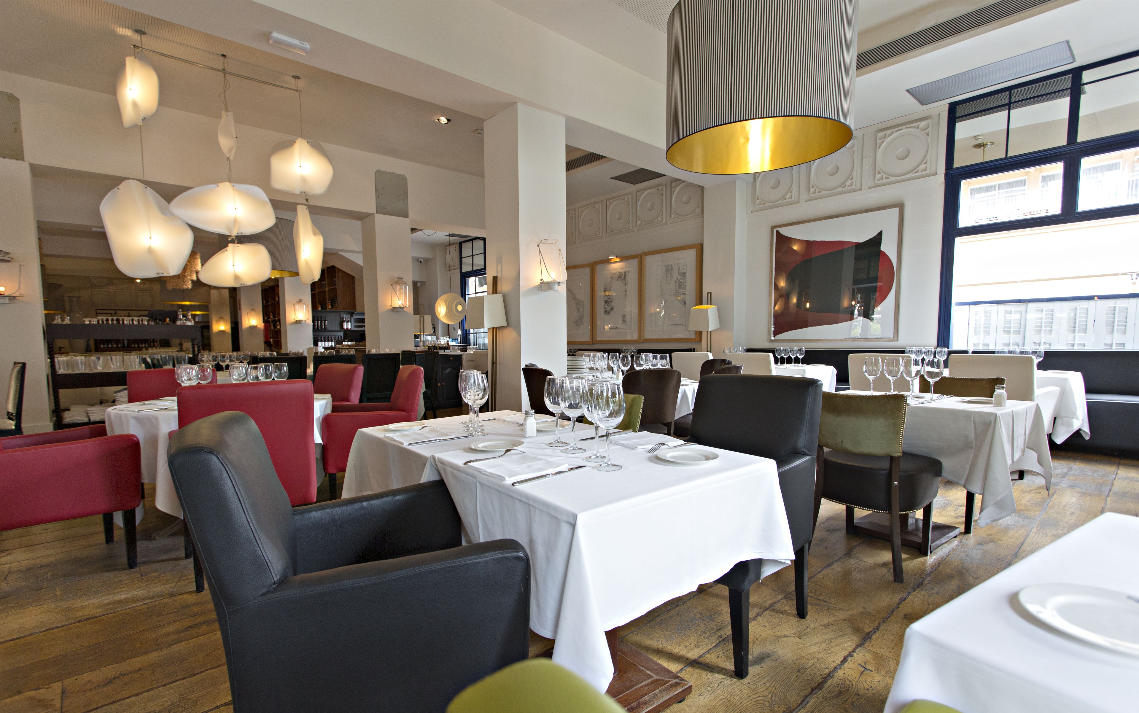 A restaurant interior with tables set for dining, pendant lighting, and framed artwork on the walls.