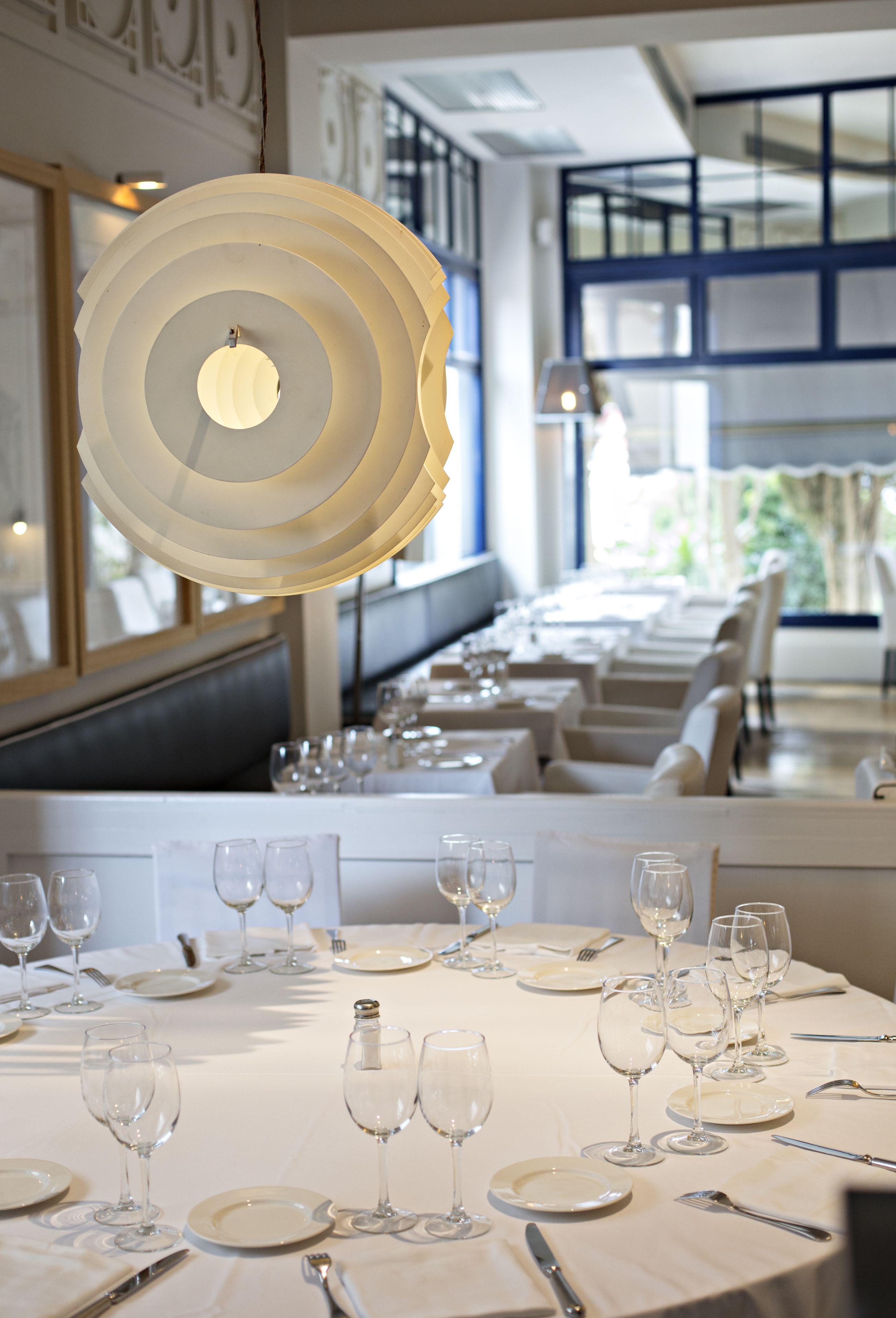 A restaurant with a long dining table set with white tablecloths, plates, and wine glasses.