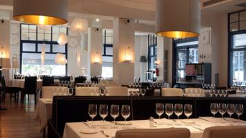 A restaurant with tables set for dining, large hanging light fixtures, and a view of the outside.