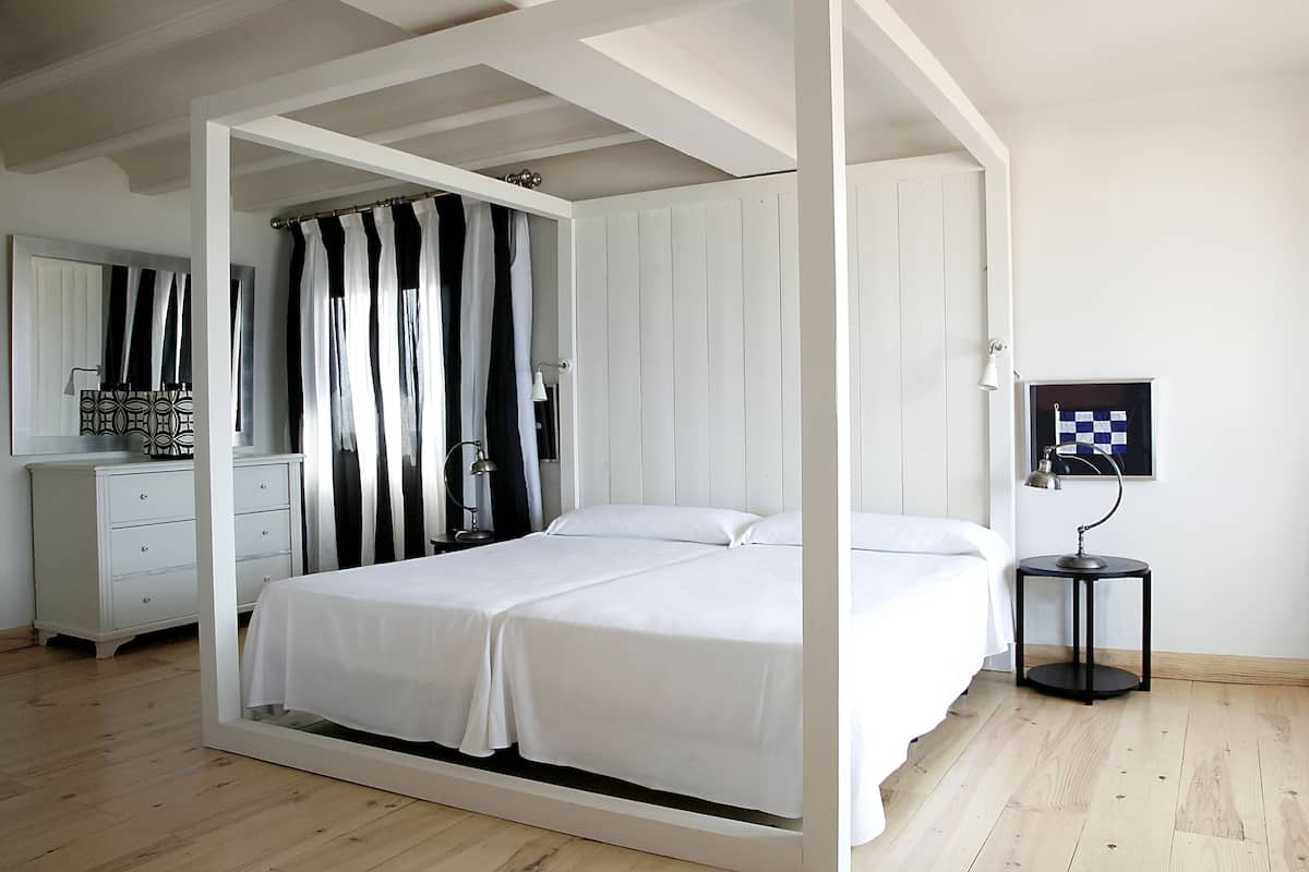 A bedroom with a bed, a dresser, a mirror, a curtain, and a small table with a lamp.