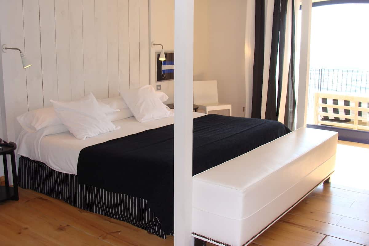 A bedroom with a bed, a bedside table, a lamp, and a view of the outside balcony.