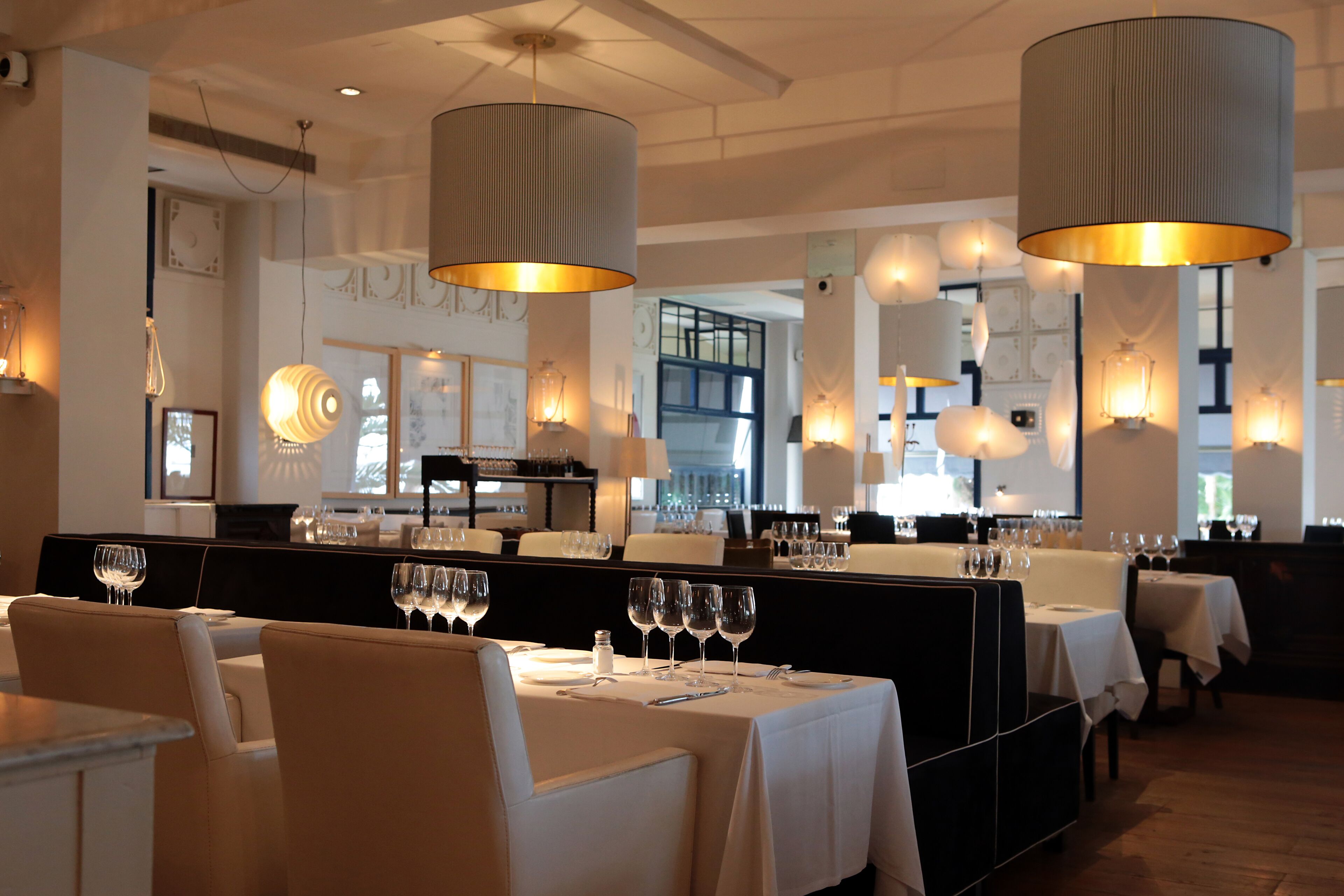 A restaurant with multiple dining tables, each set with wine glasses and cutlery, and large hanging lamps providing illumination.