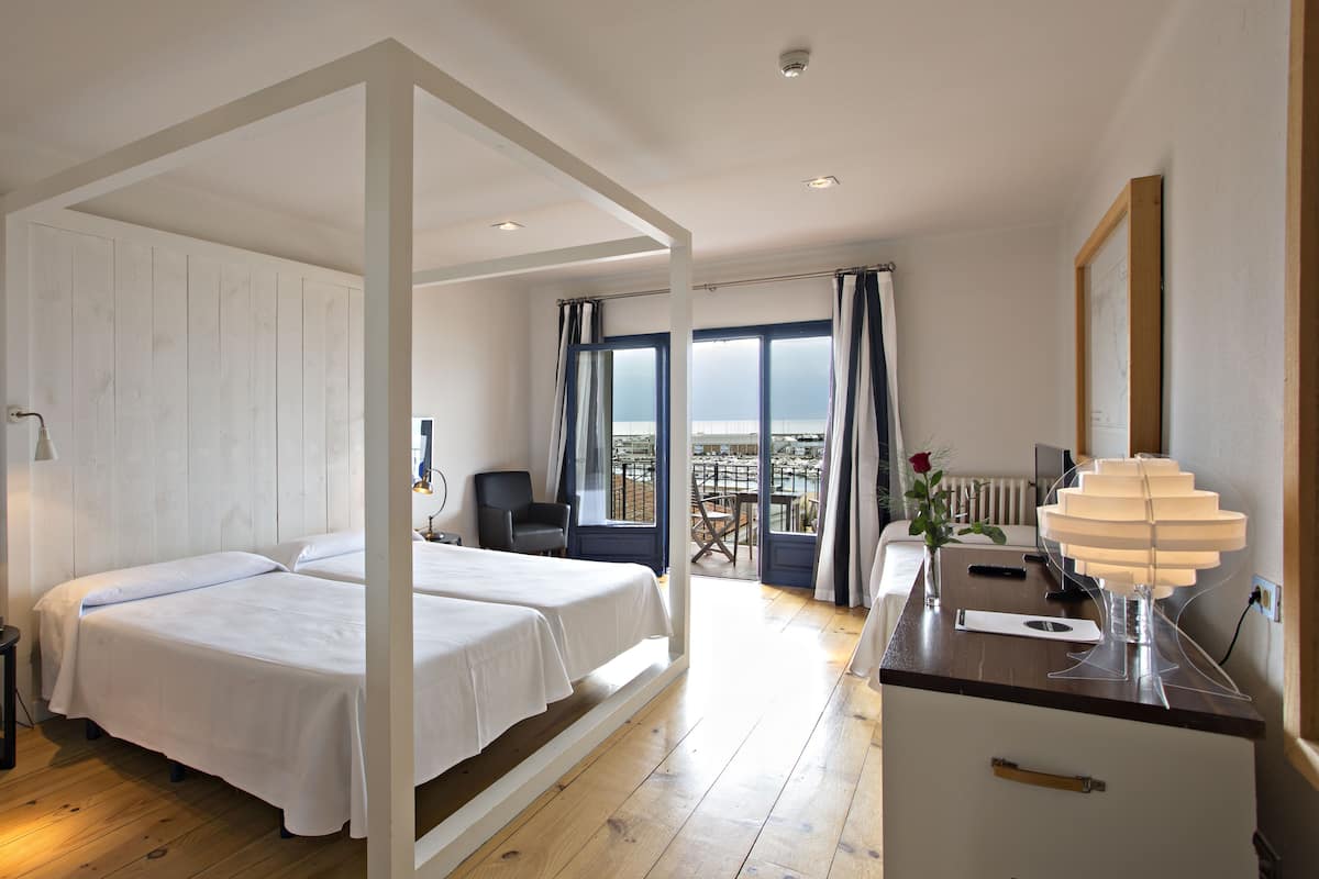A hotel room with a bed, bedside table, lamp, and a view of the city.