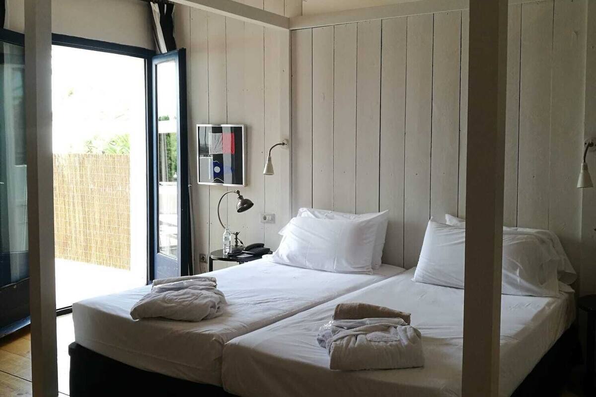 A modern bedroom with a large bed, two bedside tables, a nightstand, and a window with a view of greenery.