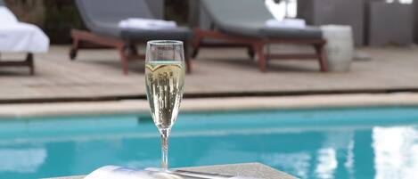 A clear view of a swimming pool with lounge chairs and a glass of champagne on a table.