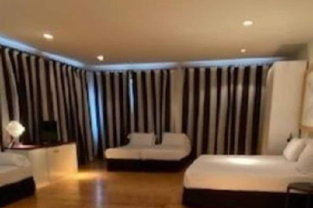 A spacious room with a large wooden floor, a bed, a sofa, and a TV on a stand.