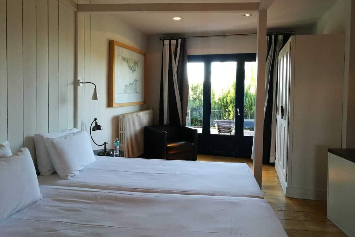 A hotel room with a large bed, a chair, a radiator, a framed picture on the wall, and a view of the outdoors through the window.