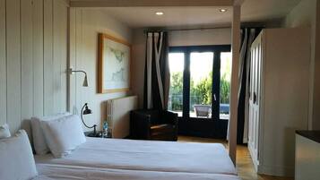 A hotel room with a large bed, a chair, a radiator, a framed picture on the wall, and a view of the outdoors through the window.