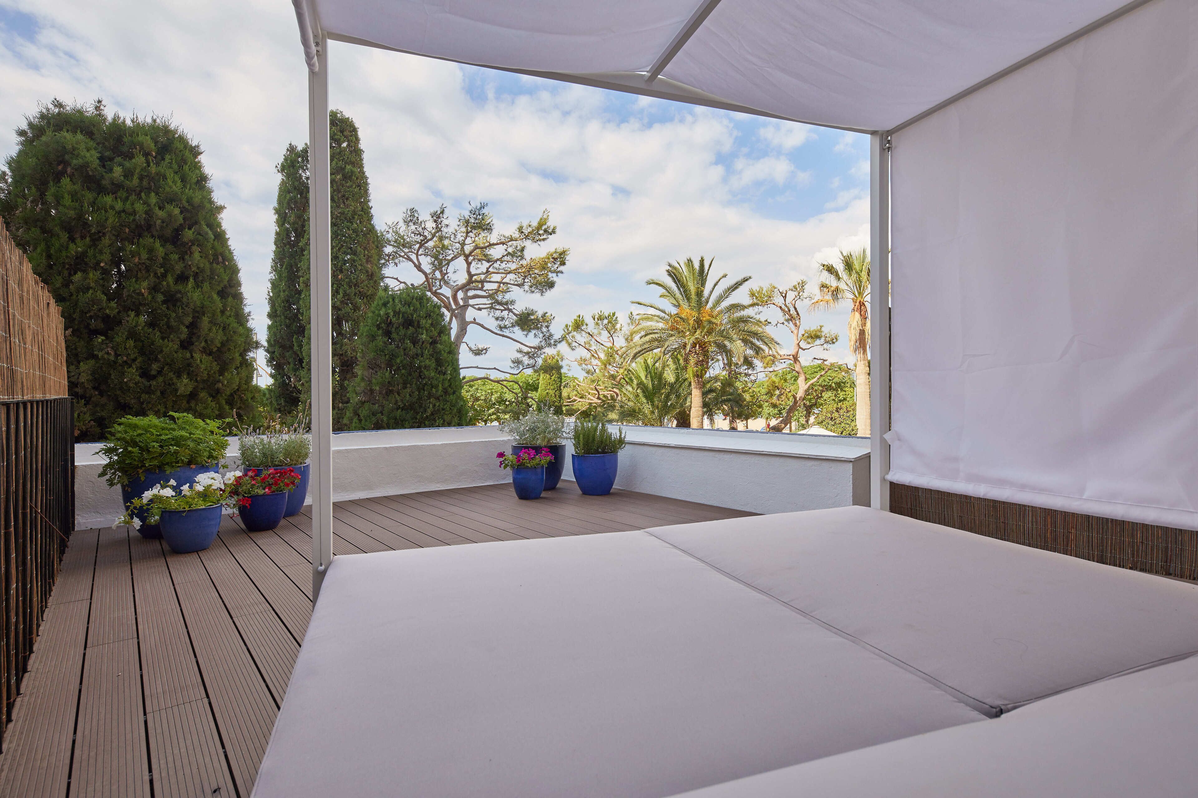 A covered outdoor seating area with a wooden deck, white cushions, and potted plants.